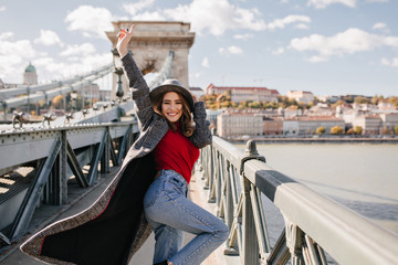 Wall Mural - carefree girl in blue jeans happy dancing on architecture background. enthusiastic curly female mode