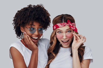 Canvas Print - Two attractive young women looking at camera and smiling while standing against grey background