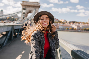 Wall Mural - enchanting lady with gorgeous curly hair posing with pleasure on bridge in windy day. outdoor portra