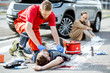 © rh2010 - Ambluence worker applying emergency care to the injured bleeding man lying on the pedestrian crossing, dispair woman driver sitting on the background