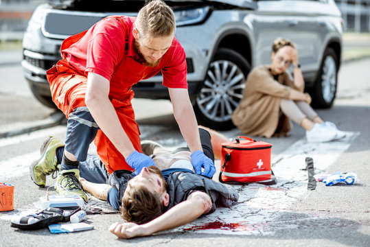ambluence worker applying emergency care to the injured bleeding man lying on the pedestrian crossin