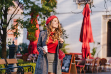 Wonderful Female Model In Gray Clothes Walking Down The Street With Cup Of Coffee. Glamorous Slim Girl In Beret Looking Away With Smile, Standing In Park.