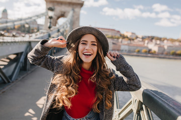 Wall Mural - gorgeous smiling woman with long curly hair posing with pleasure on bridge on blur background. outdo