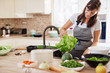 © nenadaksic - Cheerful attractive Caucasian woman in apron washing salad in kitchen. Dinner at home concept.