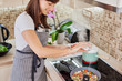 © nenadaksic - Charming Caucasain brunette in apron standing next to stove in kitchen and adding salt into braised vegetables dinner.