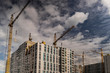 The work of construction cranes on the background of flying clouds