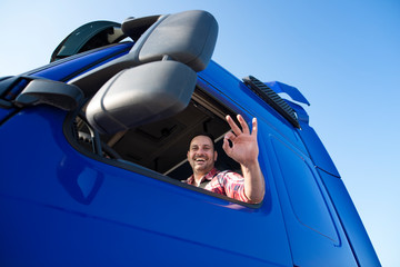 Truck driver showing okay hand gesture in his cabin. Good and fast transportation services.