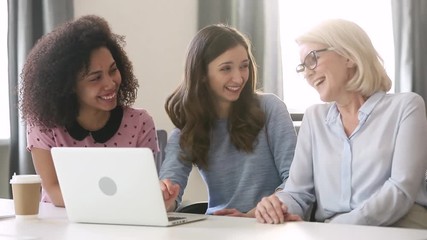 Wall Mural - Three happy diverse young old women talking laughing working together