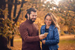 © astrosystem - Young couple using cellphone in autumn colored park.