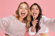 Smiling friends women posing isolated over pink wall background take selfie by camera.