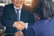 © bunyarit - Young business people shaking hands in the office. Finishing successful meeting. Businessman holding pens and holding graph paper are meeting to plan sales to meet targets set in next year.