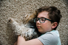 Boy Hugging His Dog Lying On The Floor At Home.