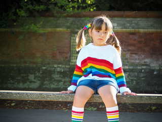 trendy little girl sitting on a wood bench in the summer park