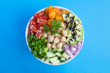 Wall Mural - Vegan poke bowl with chickpea  and vegetables in the white bowl in the center of the blue  background.Top view.Closeup.