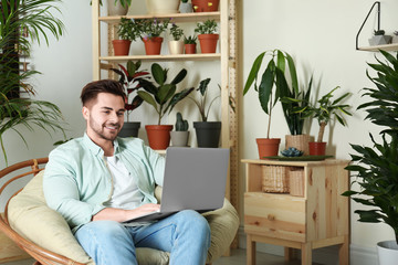 Wall Mural - Young man using laptop in room with different home plants