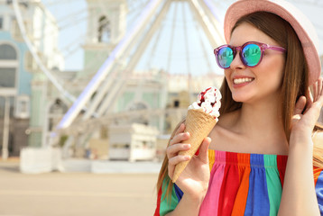 Young happy woman with ice cream cone in amusement park. Space for text