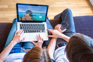 Vacation holidays planning with couple searching hotel resorts online on website for getaway destination, two people sitting on couch choosing best travel accommodation deals