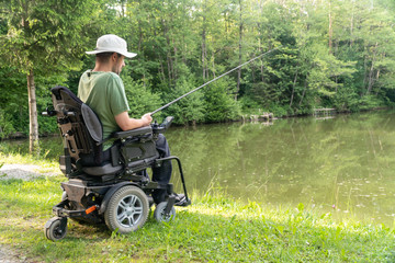 Wall Mural - Happy man in a electric wheelchair fishing at the beautiful pond in natue on a sunny day