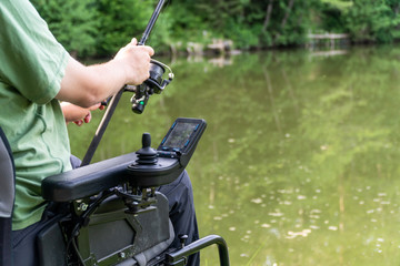 Wall Mural - closeup of a man in a electric wheelchair fishing at the beautiful pond in natue on a sunny day