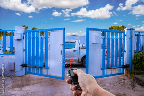 Fotomural Man used hand remote control to open swing gate door by motor automation is home security system with blue cloud sky background