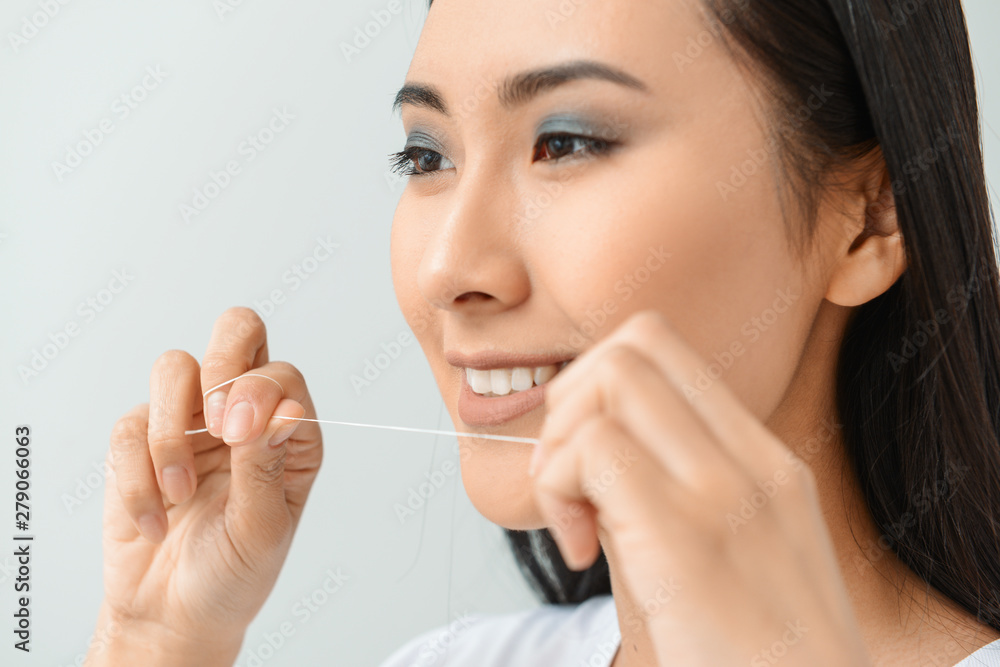 Beautiful Asian woman with dental floss on light background