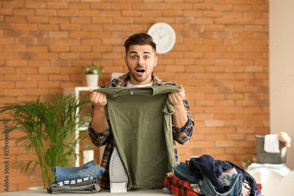 Shocked young man ironing clothes at home
