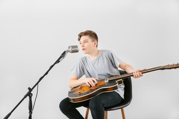 Wall Mural - Teenage boy playing guitar and singing against light background