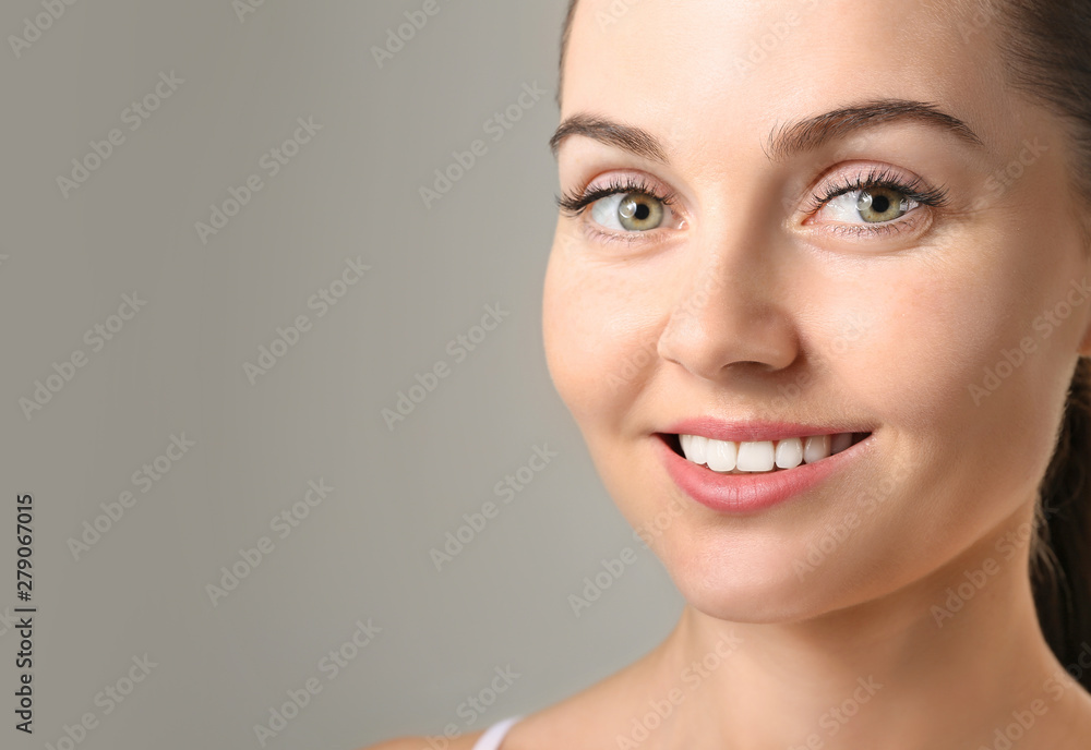 Beautiful young woman with eyelash extensions on grey background
