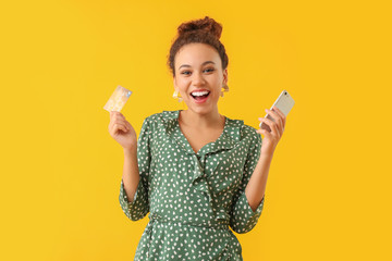 Wall Mural - Happy African-American woman with credit card and mobile phone on color background