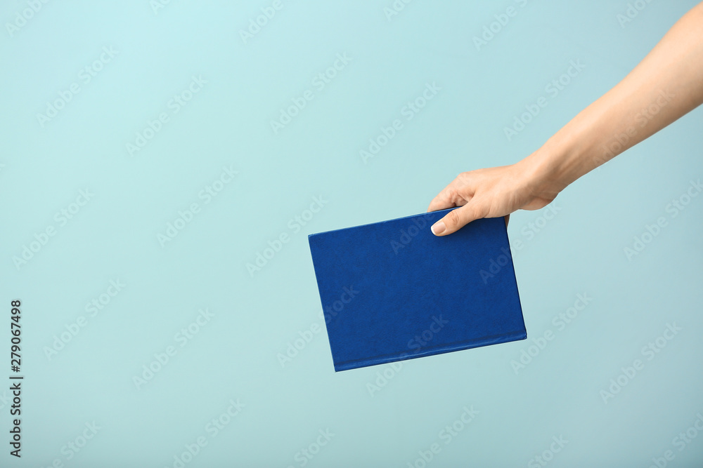 Female hand with book on color background