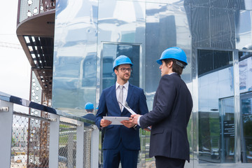 Real estate developers in helmets. New office construction. Confident business men and architect talking in front of modern office building.