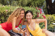 © JeanPaul - Two beautiful smiling women taking a picture with their cell phones, dressed in bathing suits - Yellow and red bathing suits