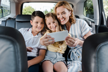 Wall Mural - selective focus of cheerful family taking selfie on smartphone in car