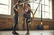 © Friends Stock - My personal trainer. Confident young man is showing slim athletic woman how to train legs with Trx fitness straps while training at gym.