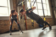 © Friends Stock - Giving motivation. Young and strong man in sportswear doing push ups with trx fitness straps and smiling while his personal trainer is standing close to him.