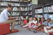 © WavebreakMediaMicro - Teacher reading a story to school kids holding a book to follow her