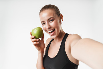 Sticker - Cheery blonde sports fitness woman posing isolated over white wall background take selfie by camera holding apple.