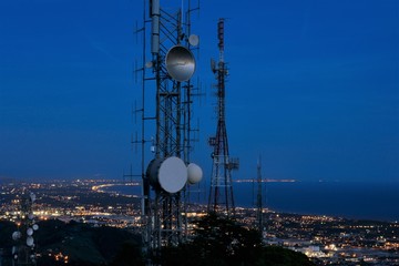 Telecommunications tower, antenna and satellite dish and coastline at night as background. Cellular station for smart city connect, aerial view.