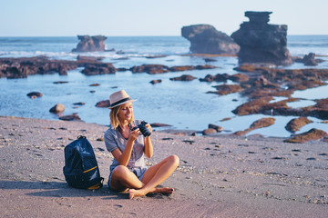 Wall Mural - Sea vacation and hobby. Pretty young woman with camera and rucksack on the ocean beach.