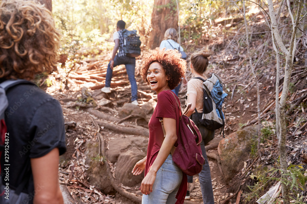 Group of millennial  friends hiking uphill on a forest trail, three quarter length - obrazy, fototapety, plakaty 