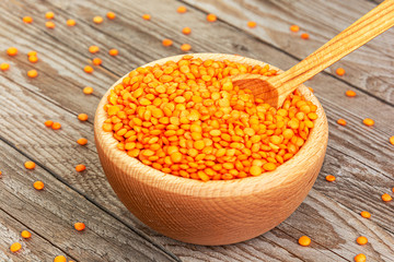 Photo of red lentils in wooden bowl with spoon on wooden background. Product photo of red lentils. Healthy lifestyle. Vegetarian and vegan diet. Spilled lens