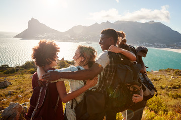 millennial friends on a hiking trip embrace at the summit to celebrate their climb, back view
