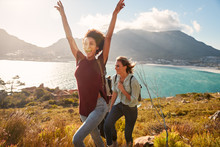 Millennial African American Woman Hiking By The Coast With A Friend Celebrates Reaching Summit