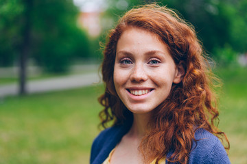 close-up portrait of beautiful young lady with long red hair and freckles smiling looking at camera 