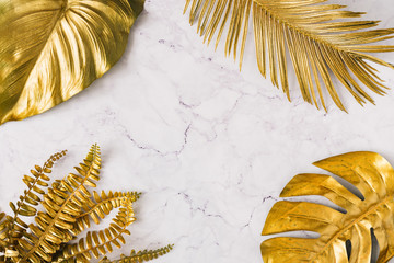 Creative layout made of golden tropical leaves and palms on white marble texture background. Minimal summer exotic concept with copy space. Border arrangement background.