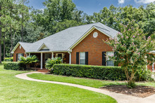 Front View Of Red Brick House In The Suburbs With A Spacious Lawn And Trees With Lots Of Curb Appeal