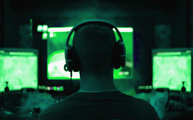 Shot of the Beautiful Pro Gamer Girl Playing in First-Person Shooter Online Video Game on Her Personal Computer. Casual Cute Geek wearing Glasses and Headset. Neon Room. eSport Cyber Games Internet