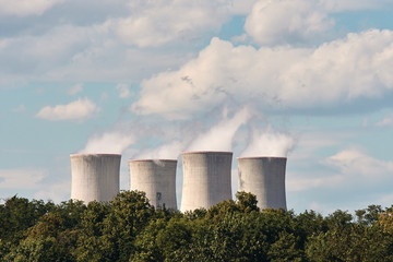 View of smoking chimneys of nuclear power plant, power lines and forest, under blue sky with clouds