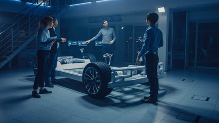 Fototapete - Automobile Engineers Working on Electric Car Platform Chassis, Using Tablet Computers with CAD Software for 3D Concept. In Automotive Innovation Facility Vehicle Frame with Wheels, Engine and Battery