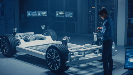 Fototapete - Automobile Engineer Working on Electric Car Chassis Platform, Using Tablet Computer Augmented Reality with 3D CAD Software Modelling. Innovative Facility: Vehicle Frame with Wheels, Engine, Battery